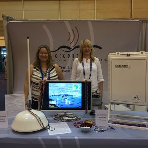 Two women stand at an exhibit booth with codar products